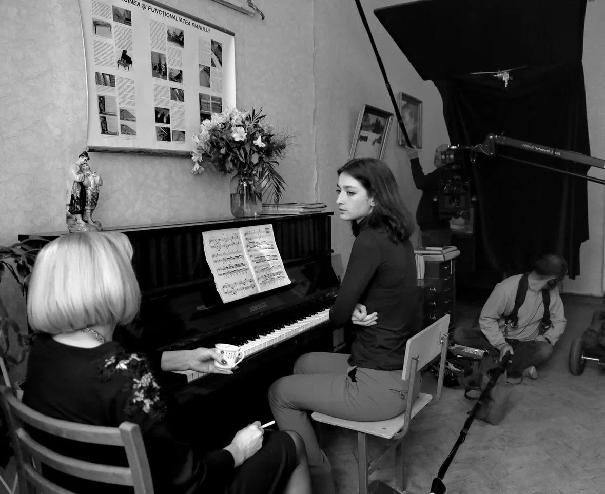 Arina Mura at the piano during a filmed scene rehearsal, crew in background