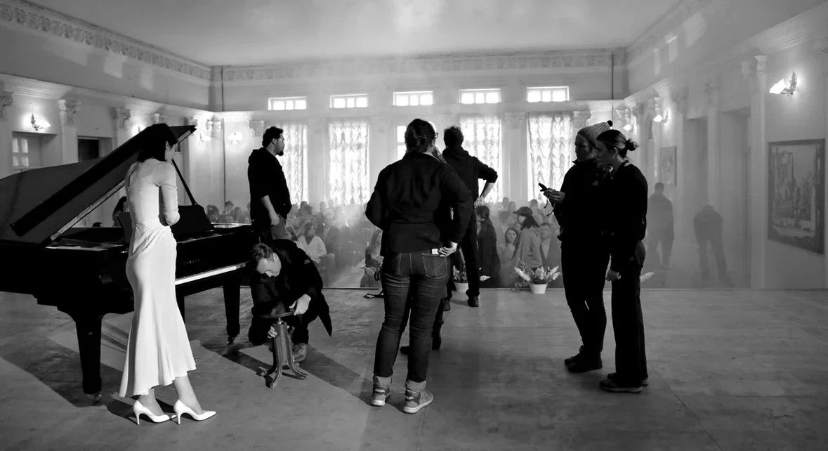 Arina Mura on set in a concert hall with film crew and haze lighting
