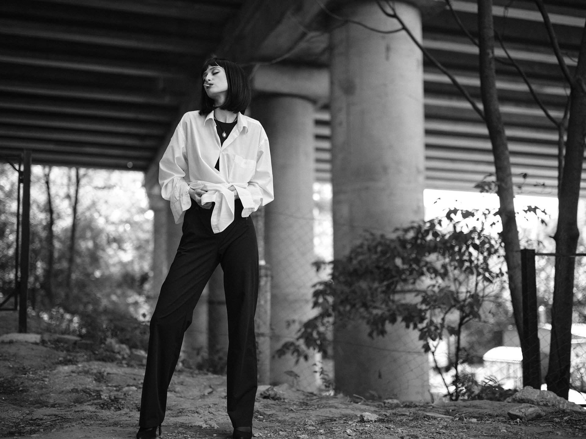 Arina Mura standing under a concrete underpass in an oversized white shirt and black trousers