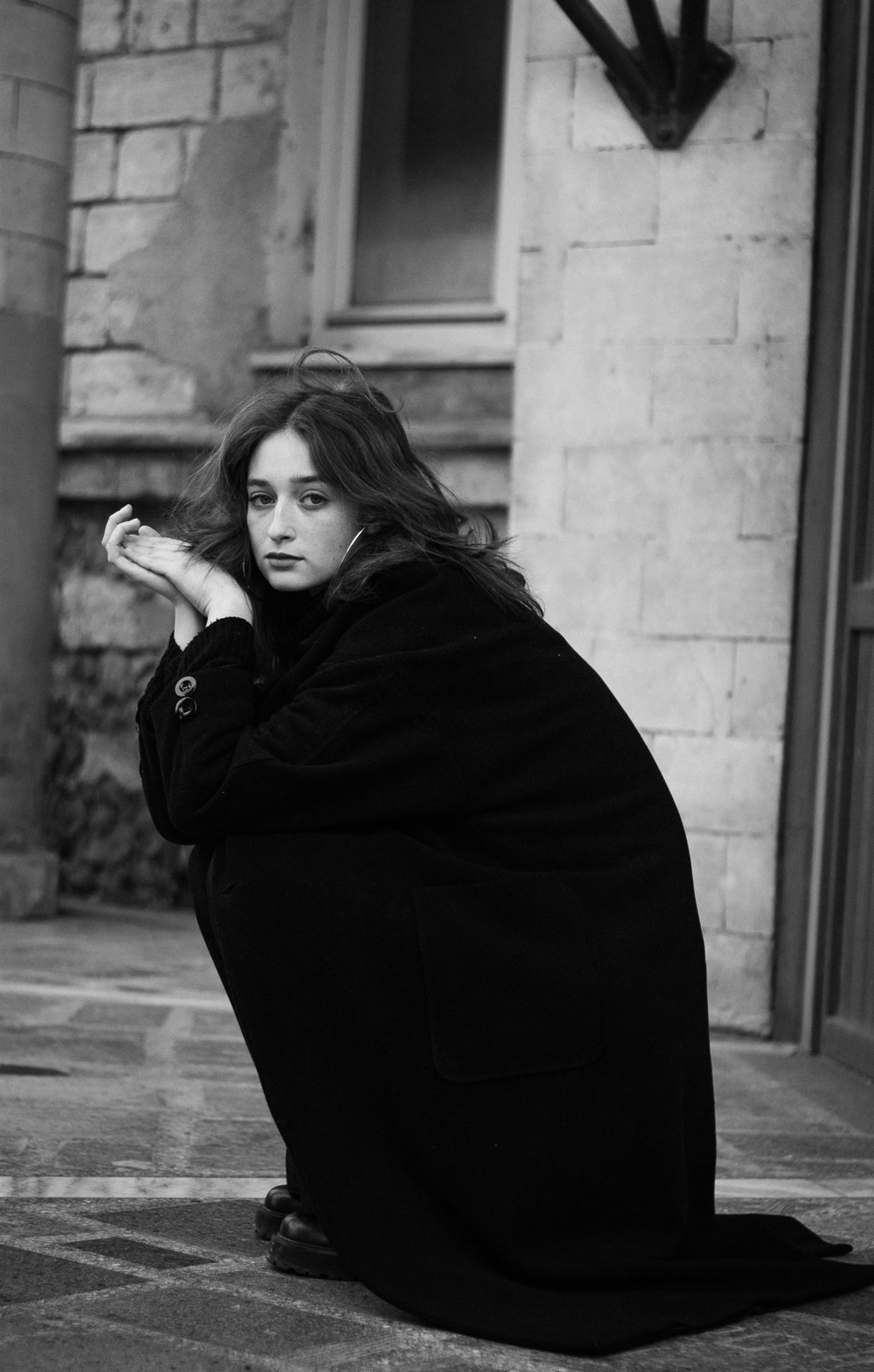 Arina Mura seated street portrait wrapped in a black coat