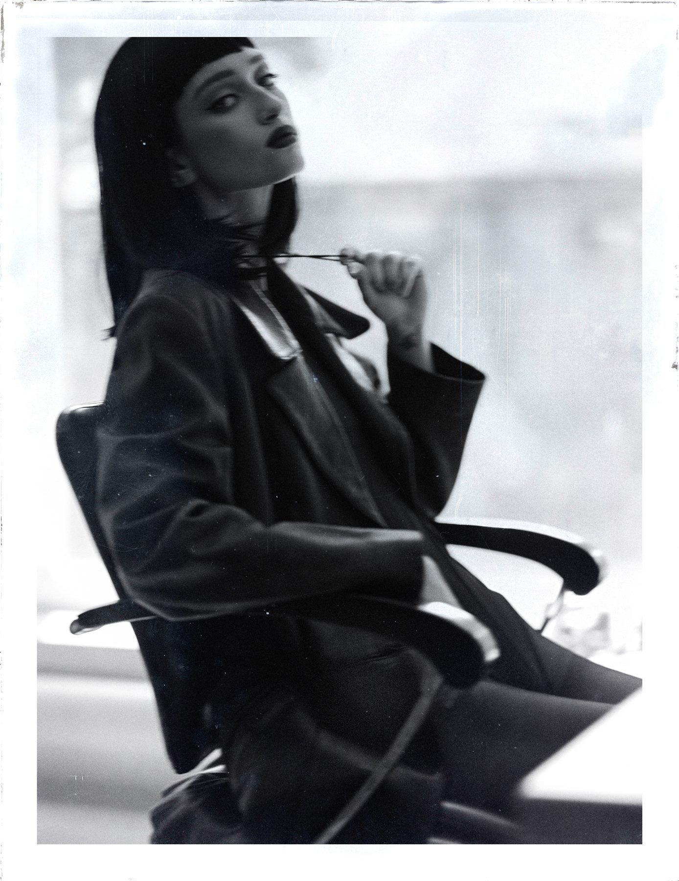 Black and white instant-film style editorial portrait of Arina Mura seated, dark bob and leather jacket
