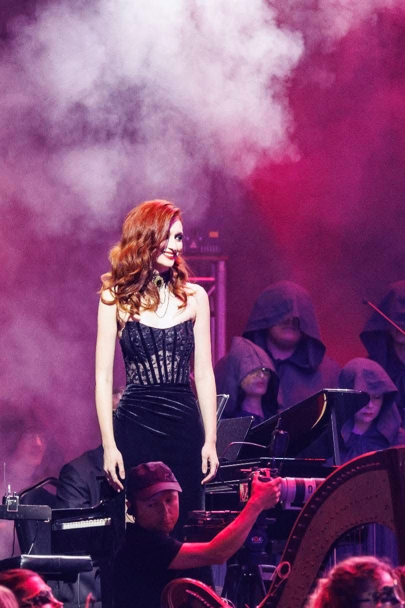 Arina Mura on stage in a black dress with orchestra and pink stage smoke